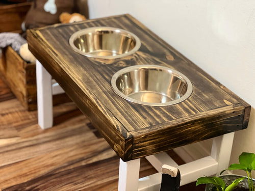 Wooden pet feeding station with two metal bowls on a wooden floor. Wooden pet feeding station with two bowls on a wooden floor. Raised dog bowl stand, dog bowl holder, large dog bowl stand, small dog bowl stand, wooden dog bowl stand raised, elevated pet bowl stand, elevated dog bowl stand, dog bowl stand wood, elevated dog bowl stand with two bowls
