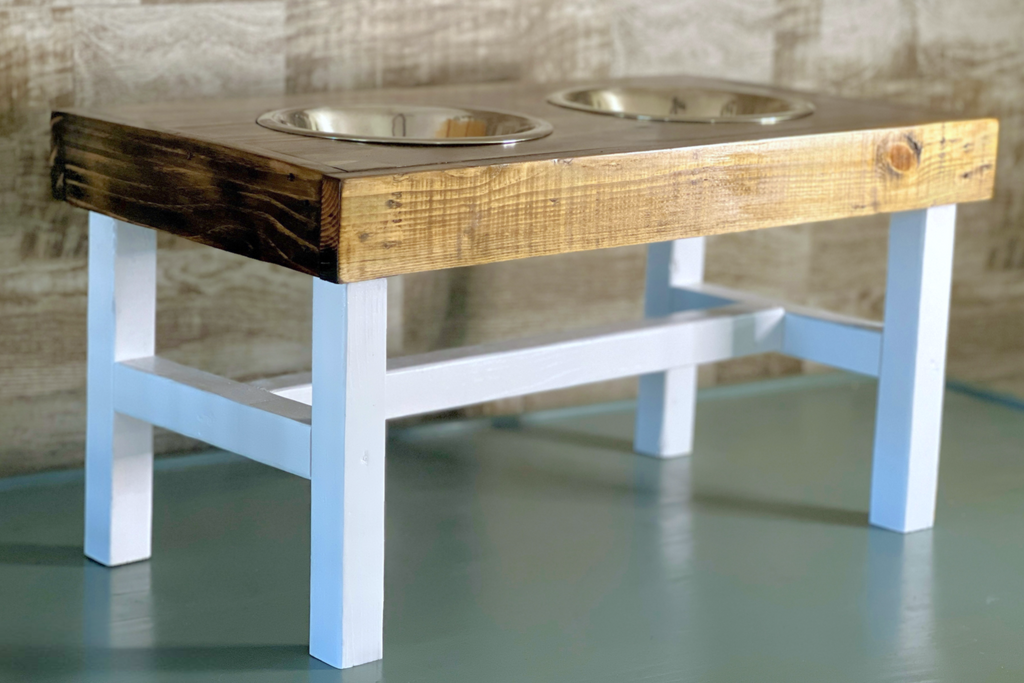 Wooden pet feeder with two bowls on a white base against a textured wall. Wooden pet feeding station with two bowls on a wooden floor. Raised dog bowl stand, dog bowl holder, large dog bowl stand, small dog bowl stand, wooden dog bowl stand raised, elevated pet bowl stand, elevated dog bowl stand, dog bowl stand wood,